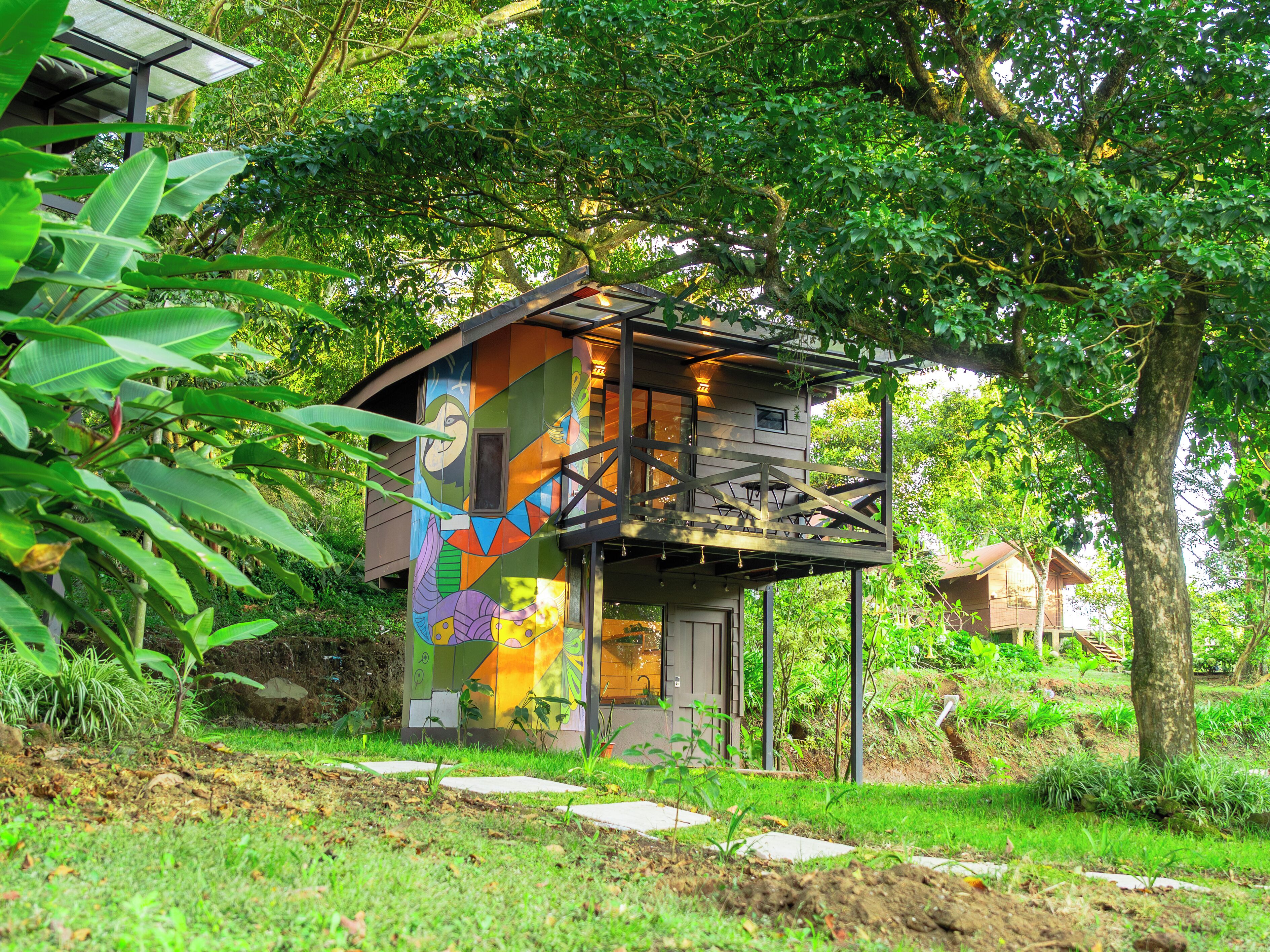 A treehouse with a colorful mural, surrounded by lush greenery and a clear sky.
