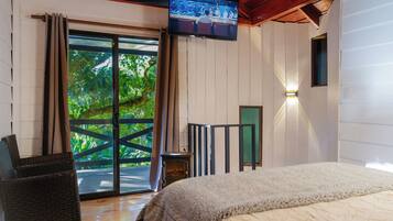 Un dormitorio con una cama grande, un televisor montado en la pared, una chimenea y vistas a la vegetación a través de la puerta corrediza de vidrio.