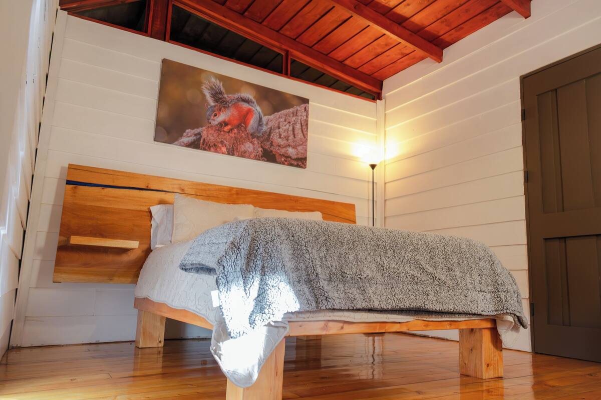 Een houten bed met hoofdeinde, een dekbed en een schilderij van een vogel aan de muur.