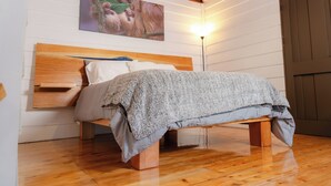 Een bed met een houten hoofdbord, een grijze deken en een houten bankvoet.
