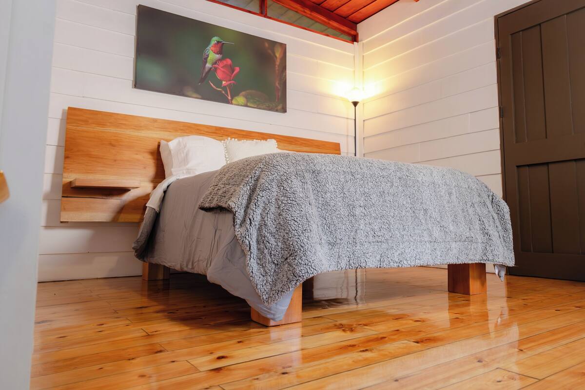 Een slaapkamer met een houten bedframe, een wit hoofdbord en een grijze deken.