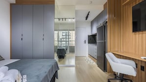 Une chambre d’hôtel moderne équipée d’un lit, d’un bureau, d’une chaise, d’une armoire et d’un coin cuisine avec un réfrigérateur et une télévision.