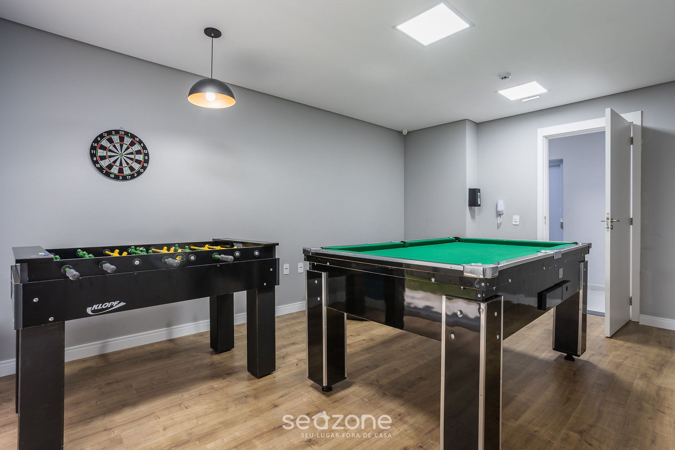A room with a foosball table, a pool table, and a dartboard on the wall.
