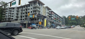 A multi-story building with balconies, a construction site, and a street with cars and traffic lights. - Stylish New 1BR Condo | Balcony, Rooftop (Port Moody)