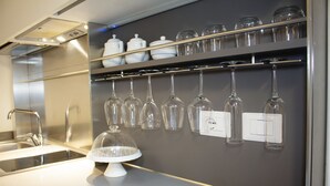 Eine Küche mit einem Edelstahlspülbecken, einer weißen Arbeitsplatte und einem wandmontierten Weinkühlschrank mit mehreren Weingläsern.