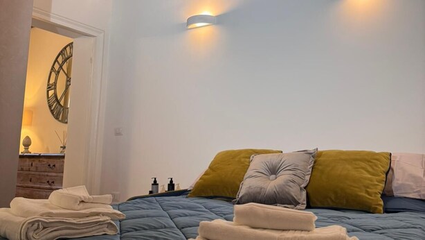 Ein Schlafzimmer mit Holzbalkendecke, einem Bett mit blauer Steudecke und zwei Wandleuchten.
