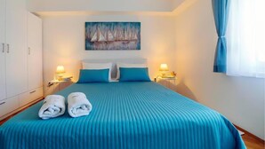 Ett hotellrum med en säng, två kuddar, två sänglampor, en tavla på väggen och ett fönster med gardiner.