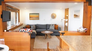 Ein gemütliches Wohnzimmer mit grauem Sofa, Couchtisch aus Holz und einem an der Wand befestigten Fernseher.