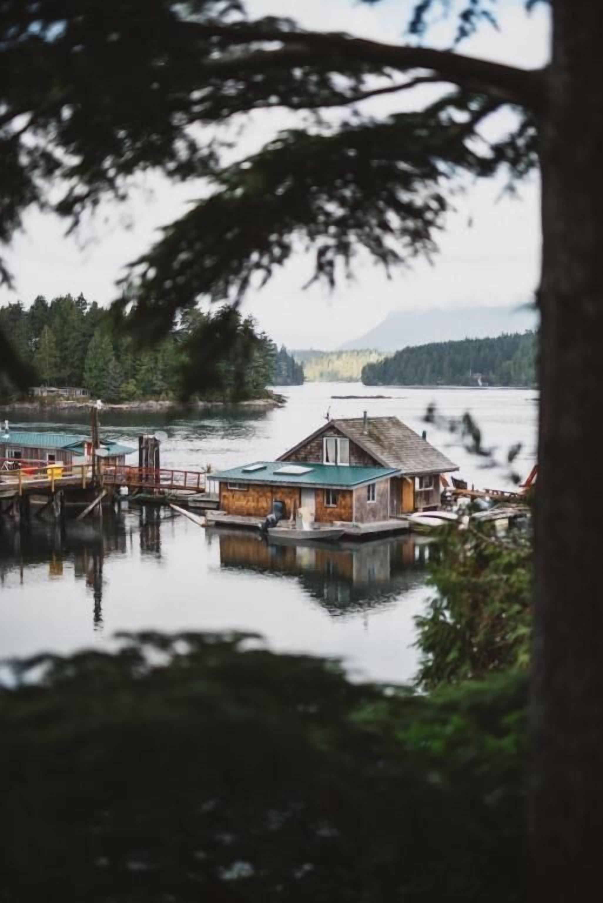Un muelle con una casa de madera y un pequeño bote, rodeado de agua tranquila y árboles.