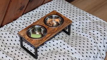 A wooden pet feeding station with two bowls on a patterned fabric.