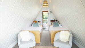 Ein gemütliches, dreieckiges Schlafzimmer im Dachgeschoss mit zwei Betten, einem großen Fenster und einer Pendelleuchte.