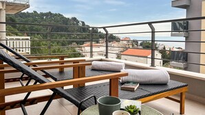 Varanda com vista para um horizonte urbano e colinas, com área de estar, uma mesa, um livro e uma xícara.