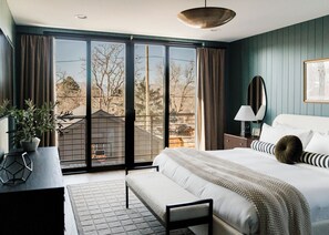 A bedroom with a large bed, a bedside table, a lamp, and a view of the outdoors through a sliding door. - Luxury 5BR with hot tub, heated game garage, mini golf, outdoor projector (Denver)