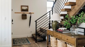 Eine Treppe mit Holzbalken und schwarzen Geländern, ein Holzkonsolentisch mit einer Lampe, eine Vase mit Pflanzen und ein gewebter Korb auf dem Boden.