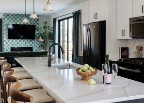 A modern kitchen with a large island, stainless steel appliances, and a flat-screen TV. - Luxury 5BR with hot tub, heated game garage, mini golf, outdoor projector (Denver)