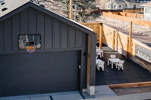 A garage with a basketball hoop, a patio with white tables and chairs, and a view of a residential area. - Luxury 5BR with hot tub, heated game garage, mini golf, outdoor projector (Denver)