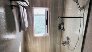 Een moderne badkamer met een glazen douchecabine, een handdoekrek met handdoeken, een raam met uitzicht op zee en een handdouche.