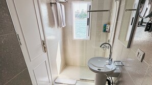 Een badkamer met een wastafel, spiegel, handdoekhouder, douche en uitzicht op de omgeving.