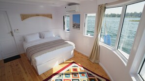 Een slaapkamer met een bed, een raam met uitzicht op het water, een deur en een airconditioning.