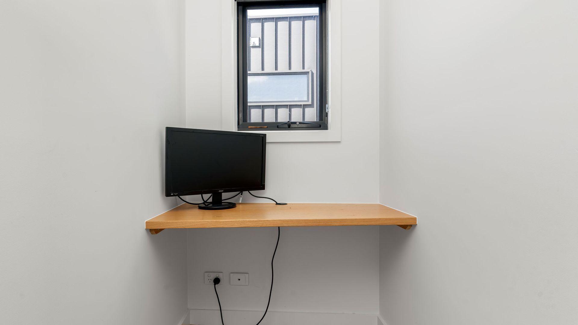 Um monitor de computador numa prateleira de madeira, com uma janela em cima.