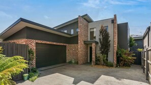 A modern two-story house with a brick facade, a garage, and a small garden with ferns. - Coastal Ember - Perfect for your next holiday!! (Inverloch)