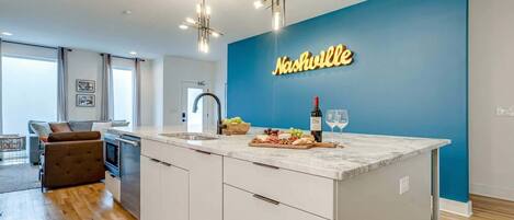 A modern kitchen with a large island, a blue accent wall, and a neon sign reading "Nashville".