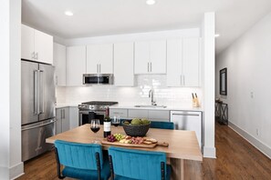 A modern kitchen with white cabinets, stainless steel appliances, and a wooden dining table with blue chairs. - Nashville home with shuffleboard game room near Belmont, sleeps 12 (Nashville)
