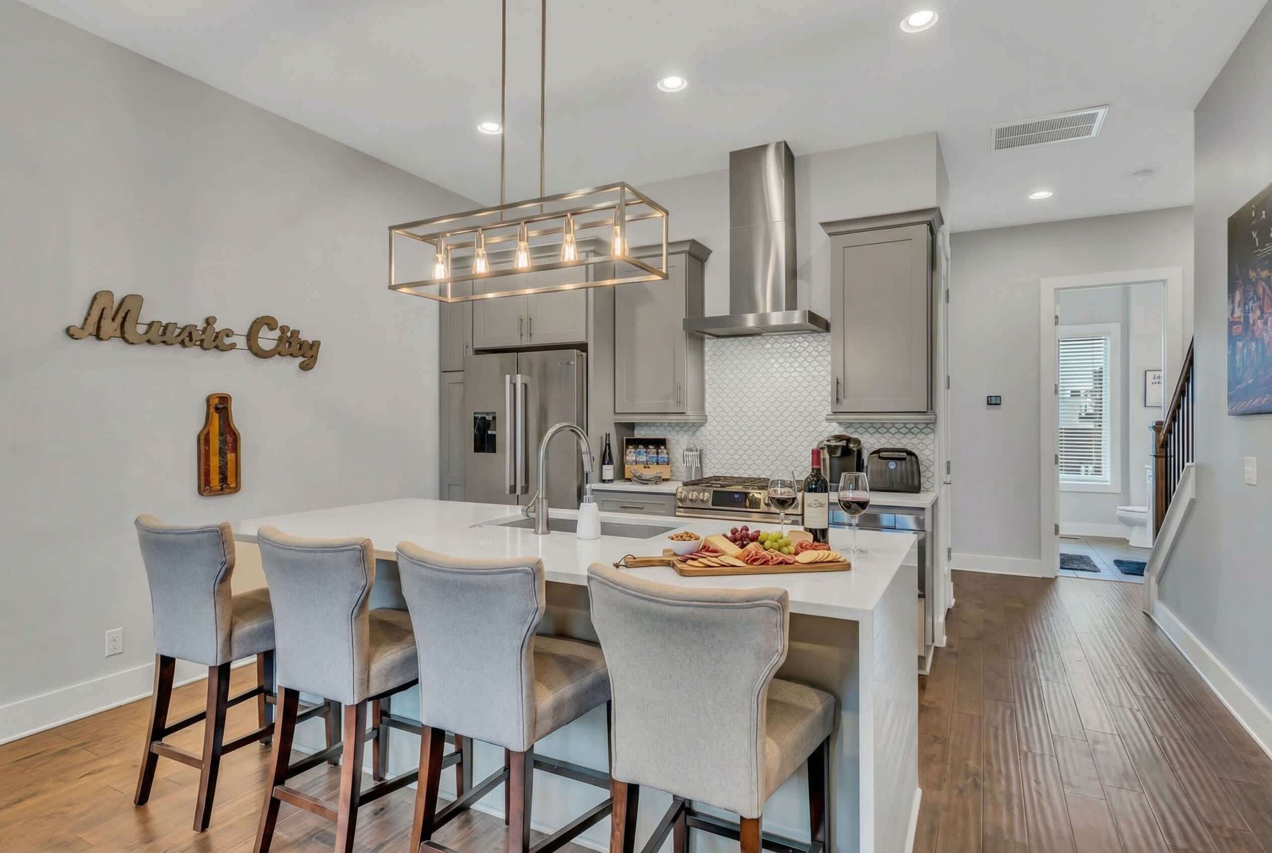 A modern kitchen with a central island, bar stools, stainless steel appliances, and a pendant light.