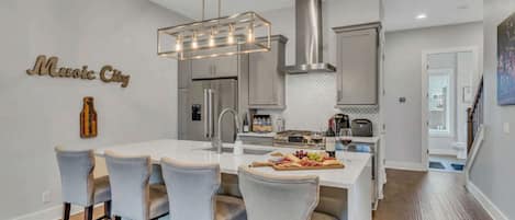 A modern kitchen with a central island, bar stools, stainless steel appliances, and a pendant light.