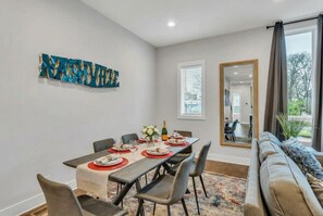 A dining area with a long table set for six, a sofa, and a large mirror. - Nashville summer getaway: rooftop deck, game room, 4br sleeps 12 (Nashville)