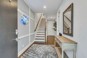 Ein Flur mit einer Holztreppe, einem Spiegel, einem Konsolentisch und einem Teppich.