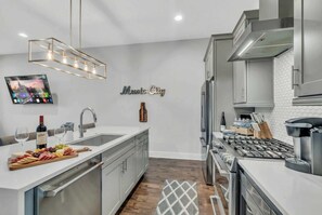 A modern kitchen with a central island, stainless steel appliances, and a wall-mounted TV. - 4-bedroom Nashville townhome sleeps 12 near Centennial Park & Parthenon (Nashville)