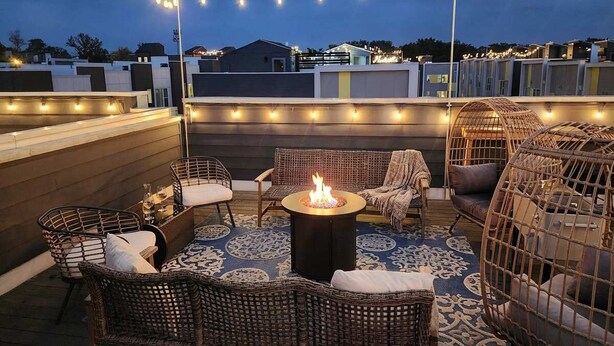 Terraza en la azotea con mobiliario de mimbre, un brasero en el centro y luces colgantes.