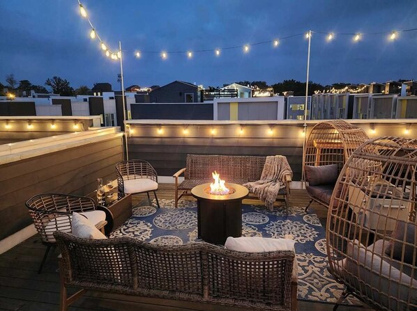 A rooftop patio with wicker furniture, a central fire pit, and string lights. - Nashville getaway home with rooftop fire pit, ping pong & sleeps 12 (Nashville)