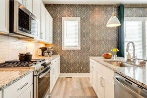 A modern kitchen with a central island, stainless steel appliances, and a geometric patterned backsplash. - Fall in Nashville: 3-story home with ping pong lounge, sleeps 12 (Nashville)