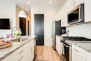 A modern kitchen with granite countertops, stainless steel appliances, and a black door. - Fall in Nashville: Ping Pong Lounge house, sleeps 12, 4 baths (Nashville)