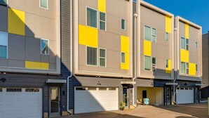 Un edificio residencial de varios pisos con un diseño moderno, que combina colores neutros y amarillos, y varios portones de garaje a nivel de calle.