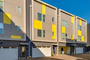 A multi-story residential building with a modern design, featuring a combination of neutral and yellow colors, and multiple garage doors at the ground level. - Nashville getaway home with rooftop fire pit, ping pong & sleeps 12 (Nashville)