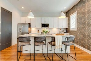 A modern kitchen with a central island, bar stools, white cabinets, and a microwave. - Nashville getaway home with rooftop fire pit, ping pong & sleeps 12 (Nashville)