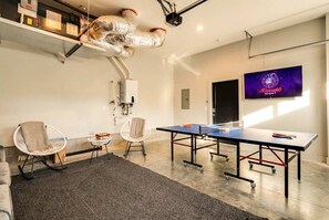 A modern conference room with a ping pong table, two chairs, a projector, and a neon sign. - Nashville getaway home with rooftop fire pit, ping pong & sleeps 12 (Nashville)