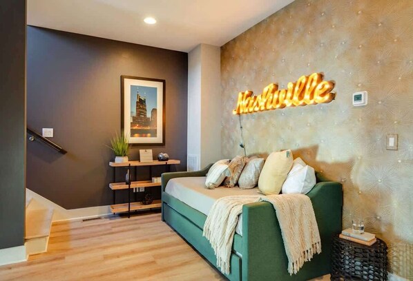 A modern living room with a green sofa, a wall-mounted neon sign, a framed cityscape picture, and a staircase. - Summer rooftop deck, ping pong lounge, skyline views near Broadway (Nashville)