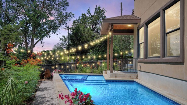 A swimming pool with a pergola and string lights, surrounded by greenery and flowers. - ATX Oasis / Pool / Firepit / Billiards (Austin)