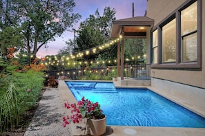 Una piscina con un pergolato e luci a tendina, immersa nel verde e tra fiori.