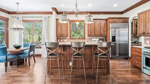 A modern kitchen with wooden cabinets, a stainless steel refrigerator, and a bar area with stools. - ATX Oasis / Pool / Firepit / Billiards (Austin)