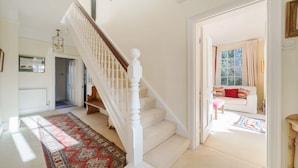 Un escalier avec des balustrades blanches et une moquette rouge à motifs menant à une pièce où se trouve un canapé blanc et un coussin rouge.