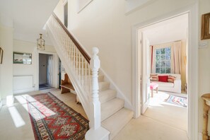 Eine Treppe mit weißen Balustraden und einem roten, gemusterten Teppich, der zu einem Raum mit einem weißen Sofa und einem roten Kissen führt.