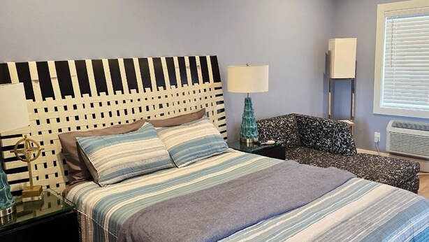 Een slaapkamer met een bed, nachtkastje, lamp, stoel en plafondventilator.