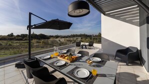 An outdoor dining area with a table set for two, a black umbrella, and a view of the countryside.