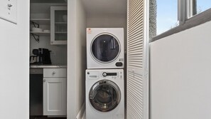 A compact laundry area with stacked washing machines, a kitchen with cabinets, and a window.
