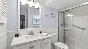 A bathroom with a white sink, mirror, and toilet, a shower with a glass door, and a towel rack.